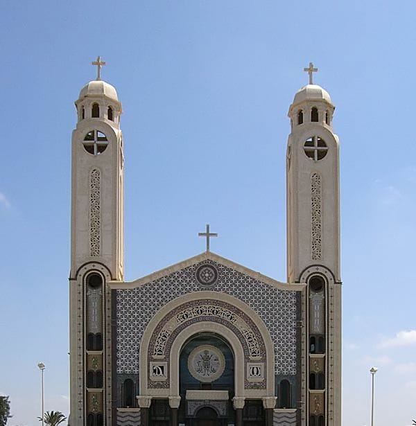 واجهة كاتدرائية دير مارمينا ببرجيها التوأمين والصلبان فوقهما، وزخارف الواجهة حول المدخل المقوس، تحت سماء زرقاء